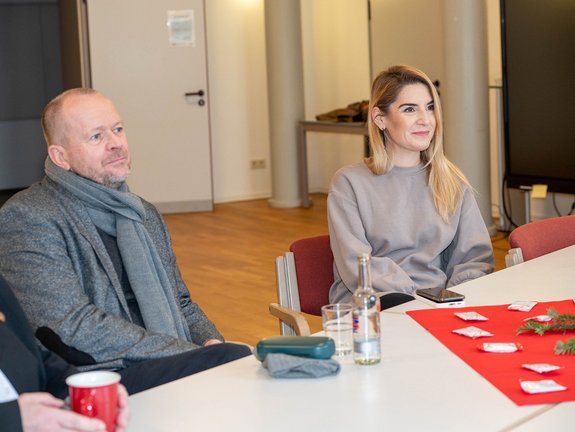 Ein Mann und eine Frau sitzen an einem weißen Tisch und hören zu.